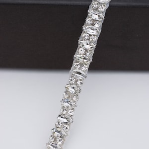 May include: A silver trim with clear, faceted rhinestones. The trim is arranged in a repeating pattern of two rows of rhinestones.