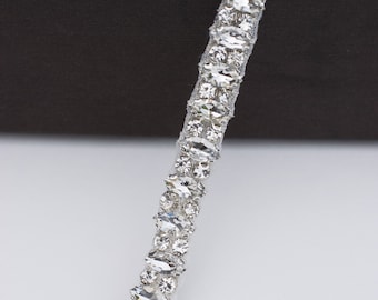 May include: A silver trim with clear, faceted rhinestones. The trim is arranged in a repeating pattern of two rows of rhinestones.