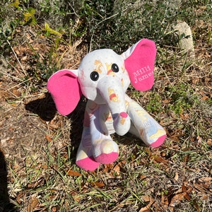 May include: A white stuffed elephant with pink ears and a Winnie the Pooh fabric design. The elephant has black button eyes and the text "Millie James" embroidered on one ear.