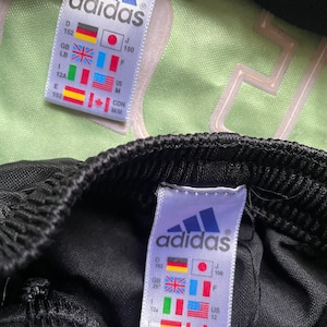 May include: Black adidas track pants with a white adidas logo and size tag. The tag shows sizes in different countries, including US size 12, Canadian size 12, and Japanese size 150.