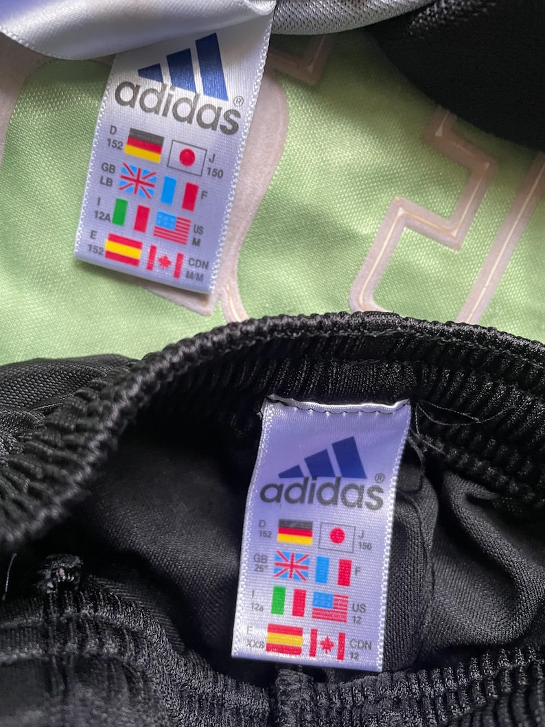 May include: Black adidas track pants with a white adidas logo and size tag. The tag shows sizes in different countries, including US size 12, Canadian size 12, and Japanese size 150.
