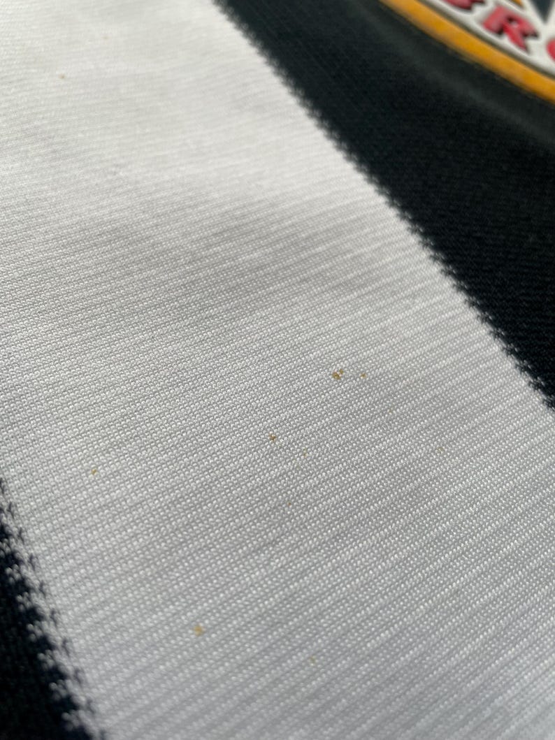 May include: Close-up of a white and black striped fabric. The fabric has a textured appearance with visible weave. The stripes are diagonal, creating a dynamic visual effect. The image is well-lit, highlighting the fabric's details.