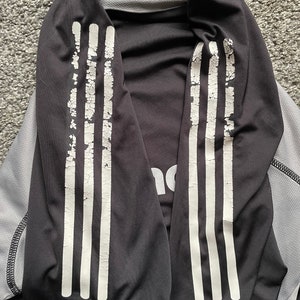 May include: Black long-sleeve shirt with white stripes on the sleeves. The shirt has the Adidas logo on the front.