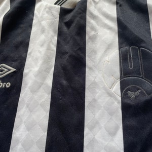 May include: Black and white striped soccer jersey with the logo "Umbro" and a team logo on the right side.