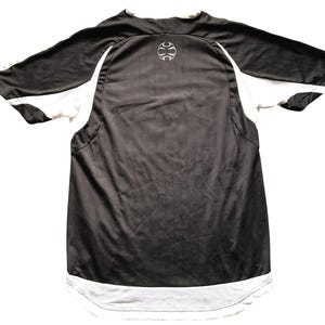 Pu&ograve; includere: Maglia sportiva bianca e nera. La maglia ha maniche corte con pannelli bianchi sui lati e un orlo in rete bianco. Un logo bianco &egrave; sulla parte superiore della schiena. La maglia &egrave; realizzata in materiale atletico traspirante.