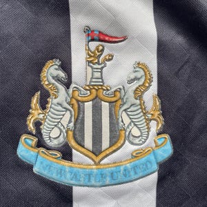 May include: Black and white striped soccer jersey with a crest featuring a shield with a black and white striped design, two seahorses, and the text "NEWCASTLE UNITED".