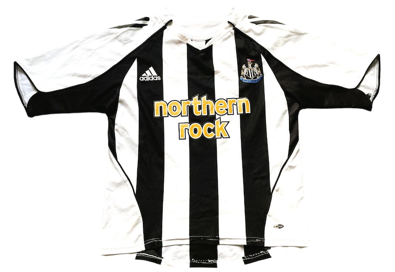 May include: A white and black striped soccer jersey with the Adidas logo on the left chest and the Newcastle United crest on the right chest. The jersey has "northern rock" written in gold letters across the chest.