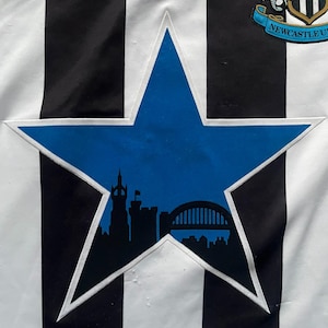 May include: A black and white striped jersey with a blue star-shaped emblem. The emblem features a silhouette of a city skyline. The jersey also has a team logo and the word "ICS" on the upper left.