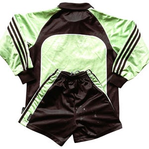 May include: A black and green soccer jersey and shorts set. The jersey has a polo collar and three black stripes on each sleeve. The shorts have a white stripe down each side.