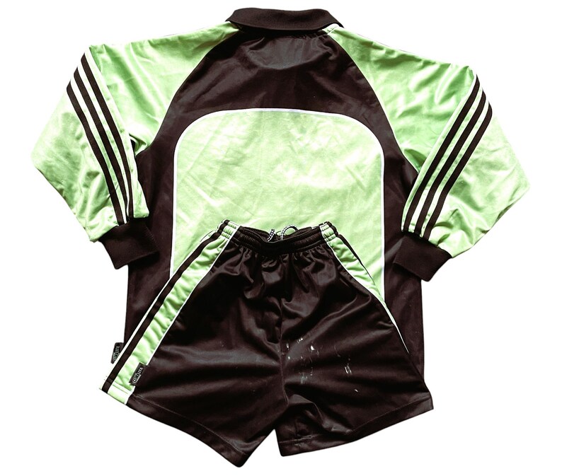 May include: A black and green soccer jersey and shorts set. The jersey has a polo collar and three black stripes on each sleeve. The shorts have a white stripe down each side.