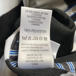 May include: White and black striped shirt tag with care instructions and information about the brand. The tag says "Die Weltmarke mit den 3 Streifen", "The Brand with the 3 Stripes", "La Marque aux 3 Bandes", "100% Polyester", "Waschen und b&uuml;geln von links", "Wash and iron inside out", "Lavage et repassage a l'envers", "Made in U.K.", "Fabrique au Royaume-Uni", and "16593".