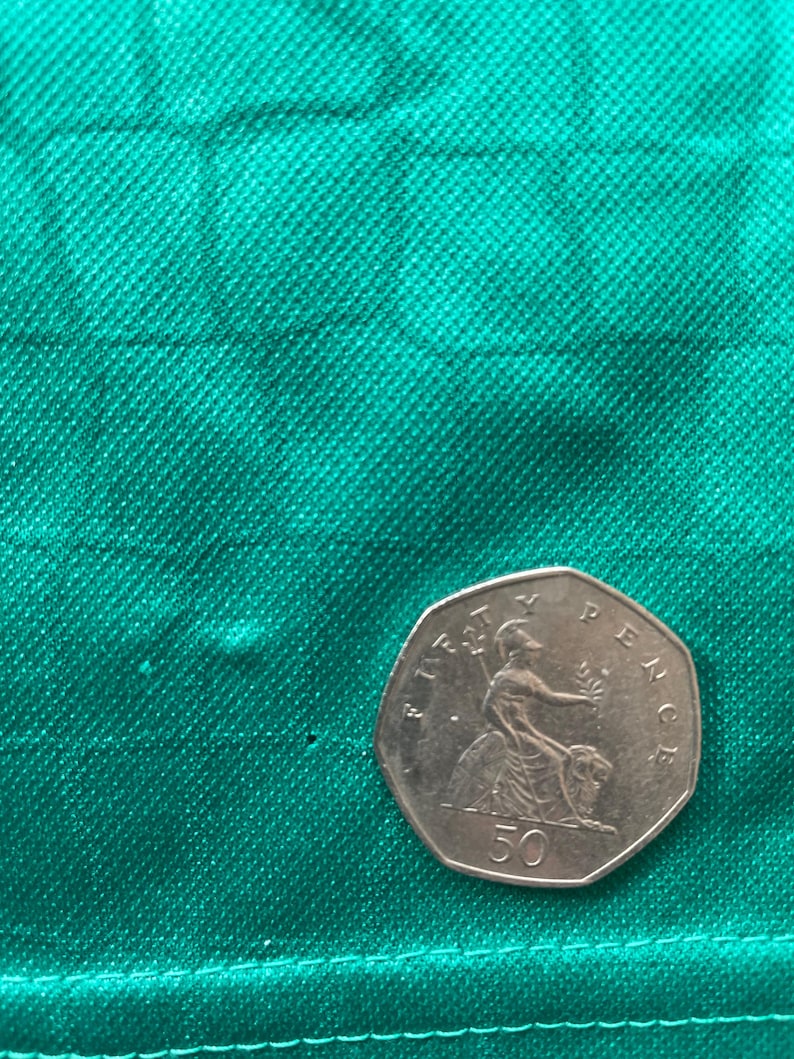 May include: A silver 50 pence coin featuring a seated Britannia figure, set against a textured green fabric background. The coin is a heptagonal shape, with the text "FIFTY PENCE" and "50" visible.