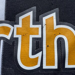 May include: Close-up of a black and white striped fabric with the word "ortho" in gold letters.