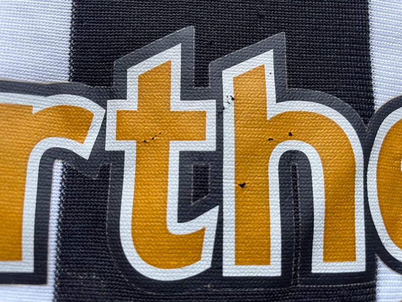 May include: Close-up of a black and white striped fabric with the word "ortho" in gold letters.