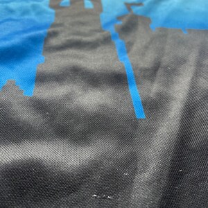 K&ouml;nnte beinhalten: Nahaufnahme eines blauen und schwarzen Stoffes mit einer Silhouette einer Burg darauf gedruckt. Der Stoff hat eine strukturierte, gewebte Optik.