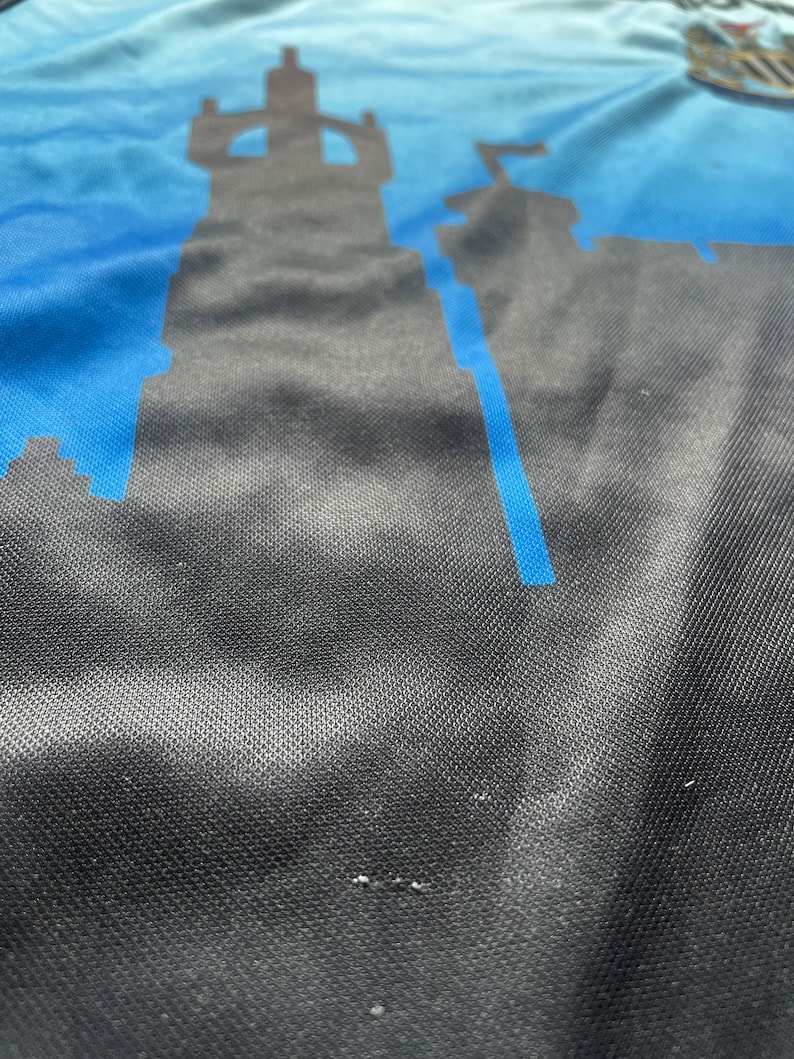 K&ouml;nnte beinhalten: Nahaufnahme eines blauen und schwarzen Stoffes mit einer Silhouette einer Burg darauf gedruckt. Der Stoff hat eine strukturierte, gewebte Optik.