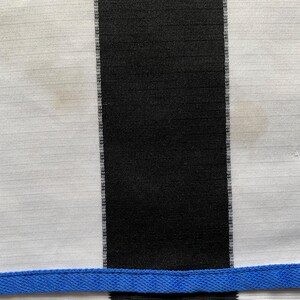May include: Black and white striped fabric with a blue trim at the bottom. The fabric has a slight sheen and is likely made of a synthetic material.