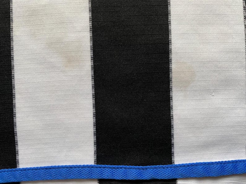 May include: Black and white striped fabric with a blue trim at the bottom. The fabric has a slight sheen and is likely made of a synthetic material.