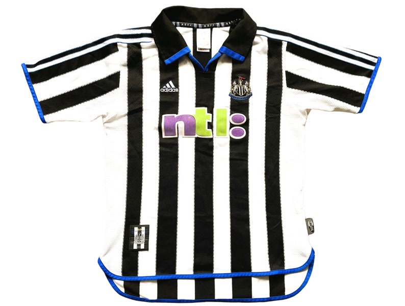 May include: A white and black striped football shirt with blue trim. The shirt has the Adidas logo, the Newcastle United crest, and the NTL logo.