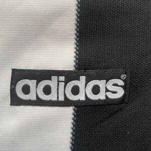 May include: Close-up of a black and white athletic jersey. The jersey is divided vertically, with a white section on the left and a black section on the right. The Adidas logo is prominently displayed on a black patch.