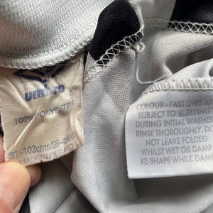 May include: White and black striped soccer jersey with a white tag that reads "100% POLYESTER 97-102cms/38-4" and a white tag that reads "COLOUR - FAST DYES ARE SUBJECT TO BLEEDING DURING INITIAL WASHES. RINSE THOROUGHLY. DO NOT LEAVE FOLDED WHILST WET OR DAMP RE-SHAPE WHILE DAMP"