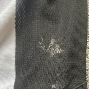 Puede incluir: Primer plano de una camiseta deportiva en blanco y negro. La camiseta tiene un panel blanco en el lado izquierdo y un panel negro en el lado derecho. Hay manchas blancas en el panel negro. La camiseta est&aacute; hecha de una tela transpirable y texturizada.