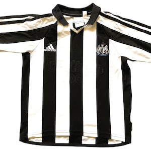 May include: Black and white striped football shirt with the Adidas logo. The shirt features a collared neckline and short sleeves with blue trim. The Newcastle United crest is visible on the chest.