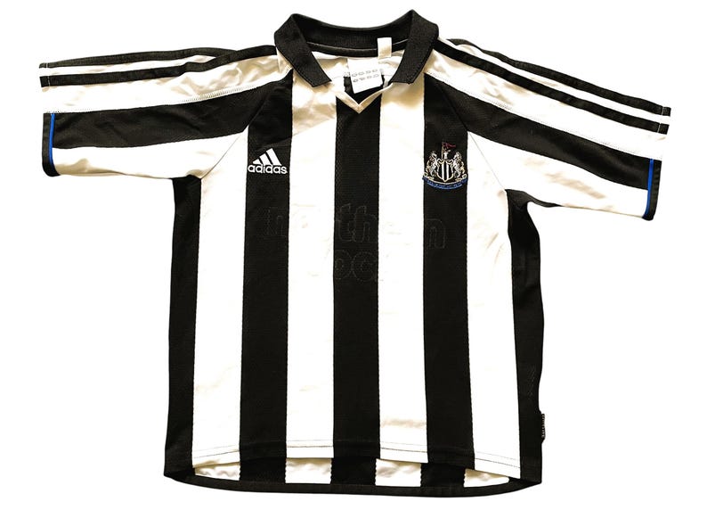 May include: Black and white striped football shirt with the Adidas logo. The shirt features a collared neckline and short sleeves with blue trim. The Newcastle United crest is visible on the chest.