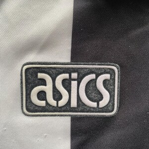K&ouml;nnte beinhalten: Nahaufnahme eines schwarz-wei&szlig;en Sporttrikots mit dem Markennamen "asics" in wei&szlig;er Schrift auf einem grauen rechteckigen Aufn&auml;her. Das Trikot hat ein vertikales Streifendesign.