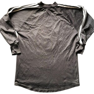May include: A dark gray long-sleeved athletic shirt with a mock neck and white stripes down the sleeves and across the shoulders. The shirt has a small logo on the lower front.