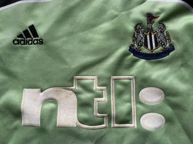 May include: A green soccer jersey with the Adidas logo, the Newcastle United crest, and the text "ntel" on the front.