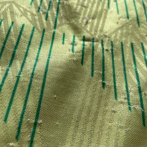 May include: Close-up of a yellow fabric with green stripes. The fabric has a textured surface and appears to be slightly worn.