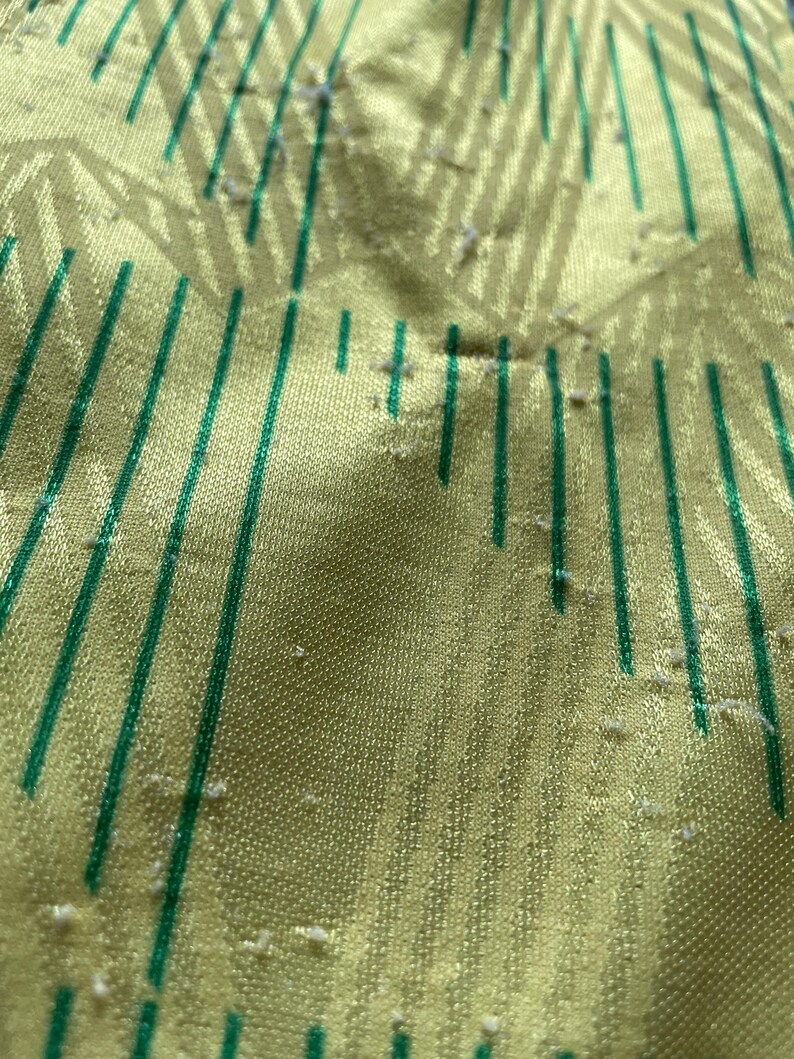 May include: Close-up of a yellow fabric with green stripes. The fabric has a textured surface and appears to be slightly worn.