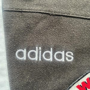 May include: Close-up of a grey sweatshirt with the word "adidas" embroidered in white on the front.