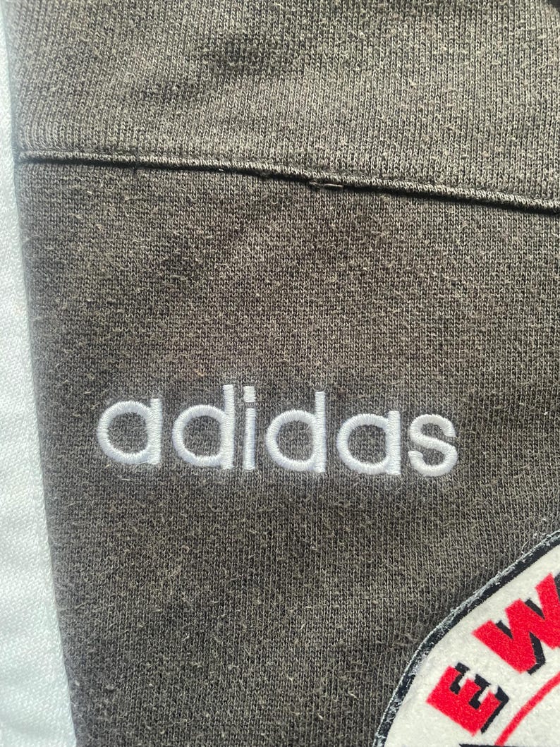 May include: Close-up of a grey sweatshirt with the word "adidas" embroidered in white on the front.