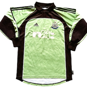 May include: A long-sleeved soccer jersey in shades of green and brown. The jersey features the Adidas logo, the text "ntl:" in white, and a team crest. The sleeves and collar are brown, while the body is green.