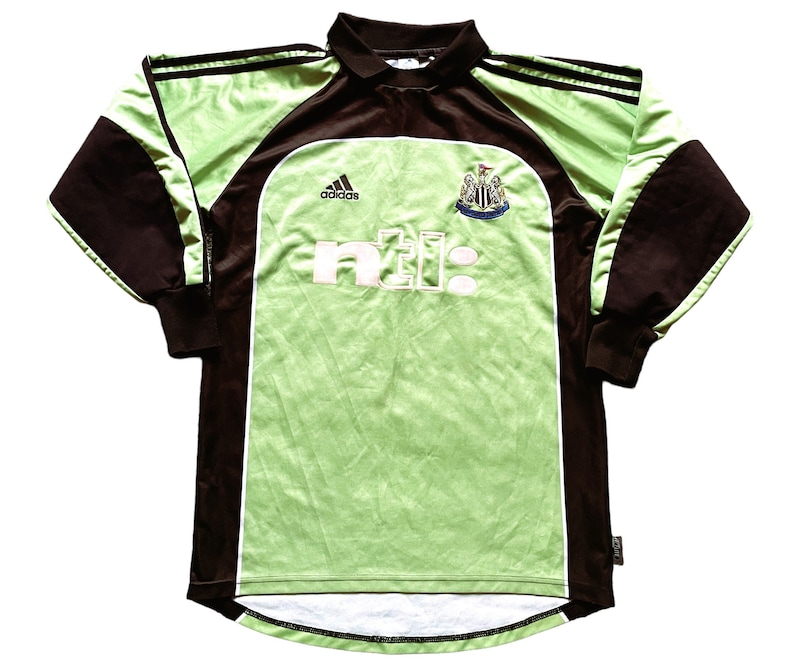 May include: A long-sleeved soccer jersey in shades of green and brown. The jersey features the Adidas logo, the text "ntl:" in white, and a team crest. The sleeves and collar are brown, while the body is green.