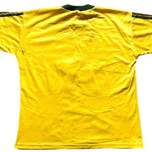 May include: A bright yellow short-sleeved jersey with a dark green collar and dark green stripes on the shoulders. The jersey is made of a lightweight, possibly athletic material, and is displayed against a white background.