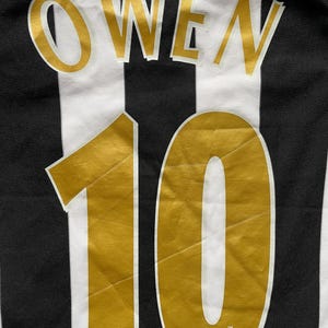 May include: A black and white striped jersey with the name "OWEN" in gold lettering above the number "10". The number is also gold. The Premier League logo is at the bottom.