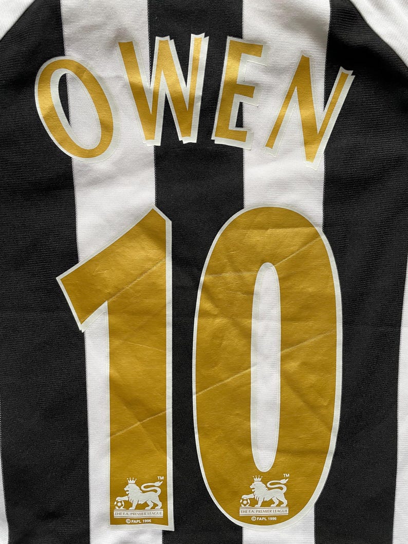May include: A black and white striped jersey with the name "OWEN" in gold lettering above the number "10". The number is also gold. The Premier League logo is at the bottom.
