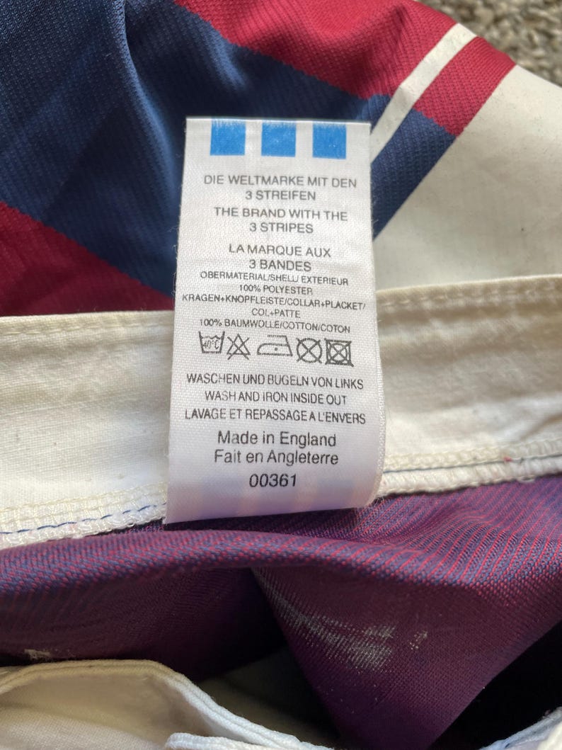 May include: A tag with text in multiple languages, including English, German, and French. The tag lists fabric composition as 100% polyester and 100% cotton. The tag also includes washing instructions and states "Made in England."