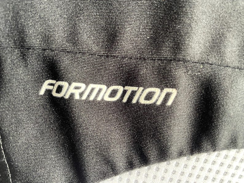 Pu&ograve; includere: Primo piano di tessuto nero con la scritta "FORMOTION" in bianco, centrata. Il tessuto ha un aspetto strutturato e le cuciture sono visibili. L'immagine &egrave; ben illuminata, evidenziando i dettagli del materiale.