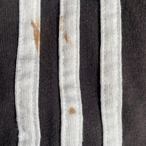 May include: Close-up of black fabric with three white stripes. There are brown stains on the fabric.