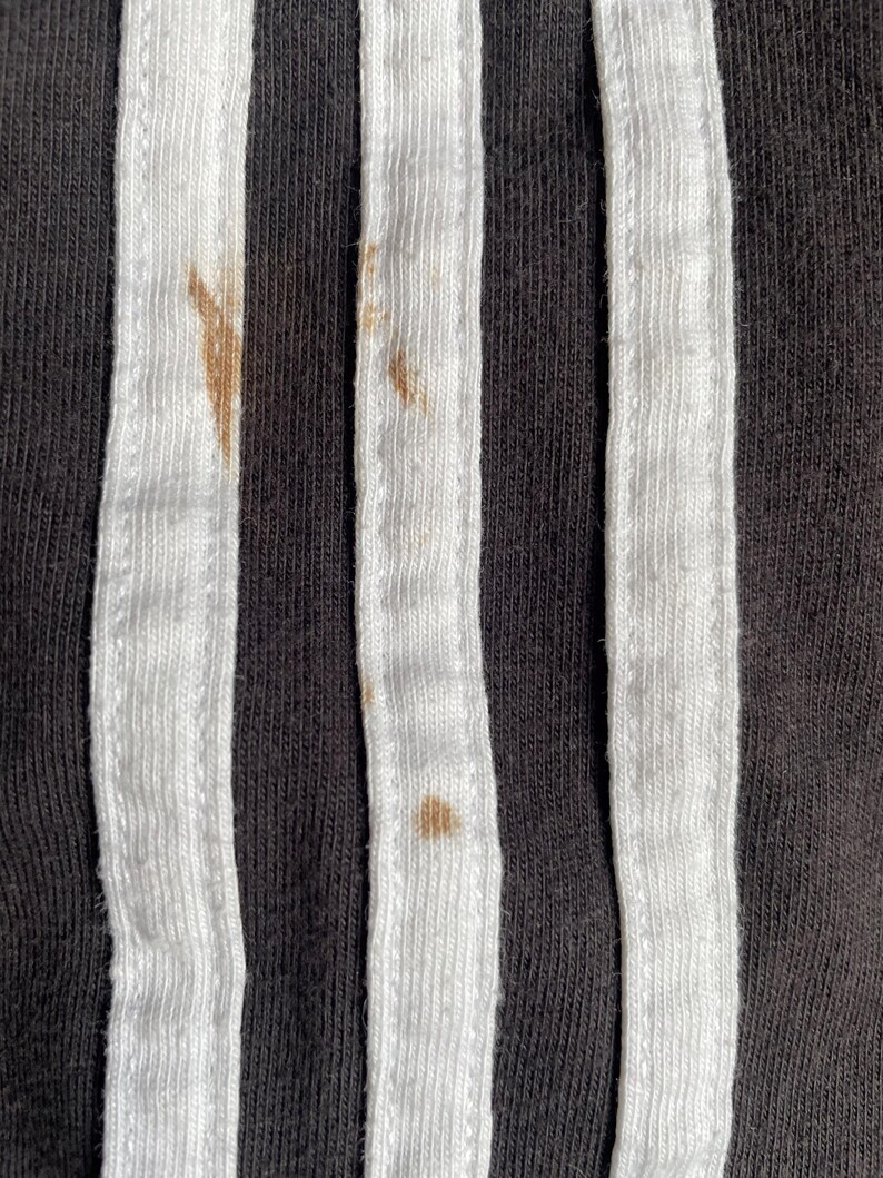 May include: Close-up of black fabric with three white stripes. There are brown stains on the fabric.