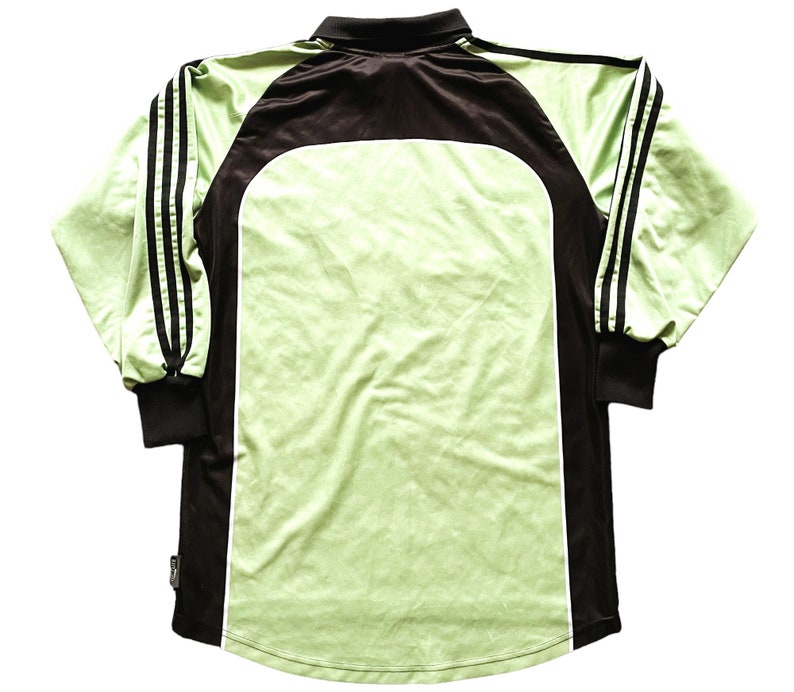 May include: A long-sleeved athletic jersey in shades of green and black. The jersey features a light green body with black accents on the shoulders, sleeves, and collar. Three black stripes run down each sleeve. The jersey has a classic athletic design.