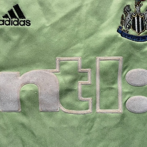 May include: Green soccer jersey with the Adidas logo, the Newcastle United crest, and the text "ntel" in white.