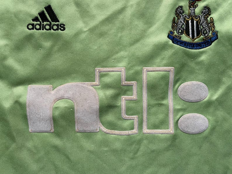 May include: Green soccer jersey with the Adidas logo, the Newcastle United crest, and the text "ntel" in white.