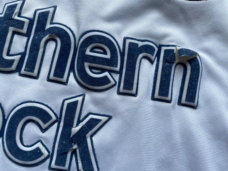 May include: Close-up of a white jersey with the text "Southern" and "ock" in navy blue lettering.