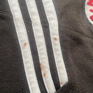 May include: Close-up of a black sweatshirt with white stripes on the sleeve. The fabric has a few brown stains.