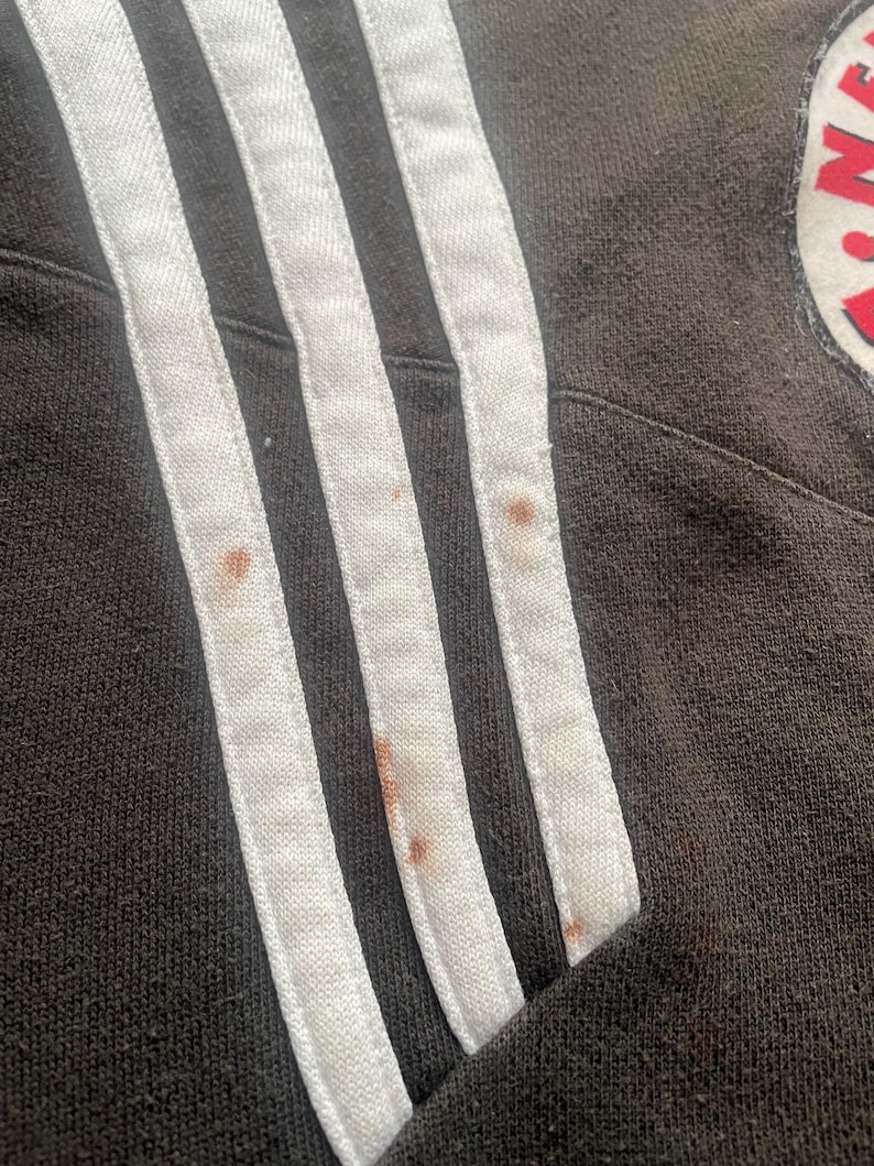 May include: Close-up of a black sweatshirt with white stripes on the sleeve. The fabric has a few brown stains.